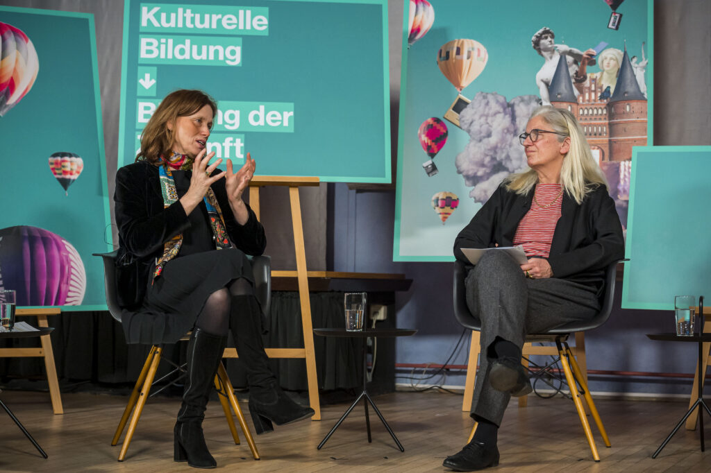 Ministerin Karin Prien und Ministerin Isabel Pfeiffer-Poensgen sitzen sich in einem Panel auf dem Forum Kreativpotentiale gegenüber und sprechen miteinander. Foto: O. Malzahn
